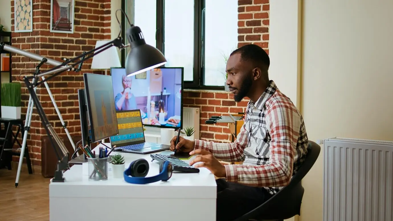 Афроамериканский мужчина-дизайнер редактирует изображения на двух мониторах.